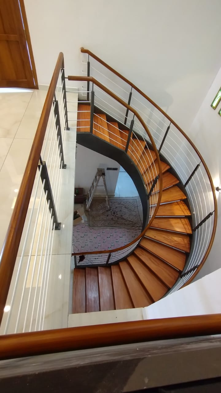Custom helical wooden-finish steel staircase fabricated in Thiruvalla, Kerala